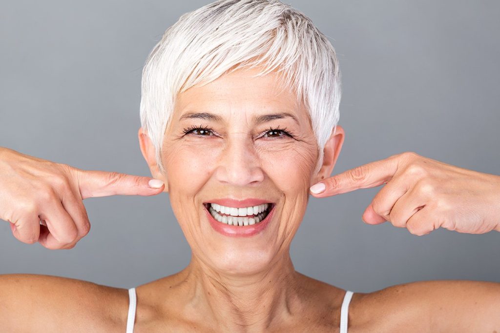 beautiful caucasian smiling senior woman with short grey hair pointing at her teeth and looking at camera beauty photography